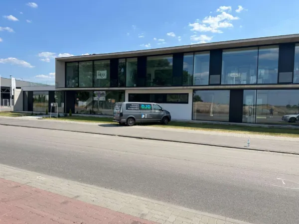 Grauer Firmentransporter vor einem modernen Glasgebäude