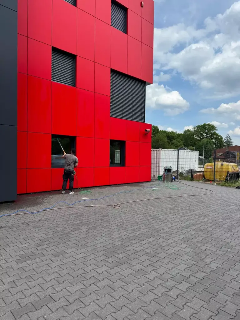 Mitarbeiter reinigt mit Teleskopstange ein Fenster einer roten Fassade