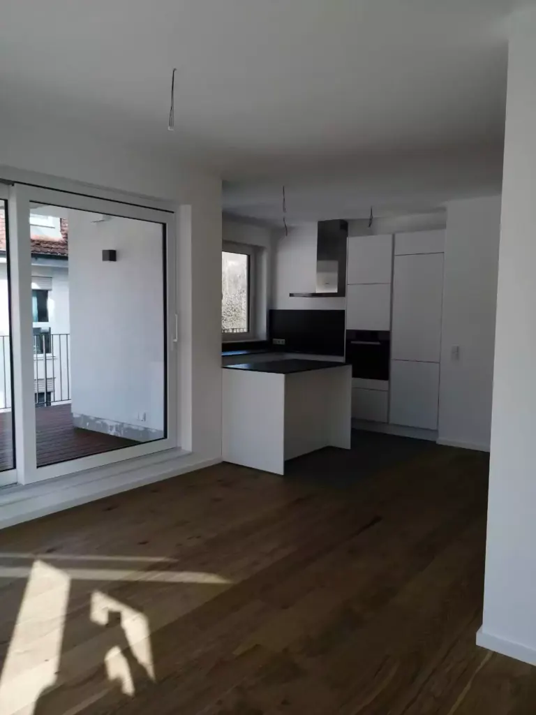 Leerer Neubau-Wohnraum mit weißer Einbauküche und Parkettboden