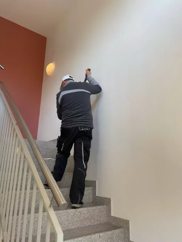 Mitarbeiter reinigt die Wand über einer Treppe im Treppenhaus