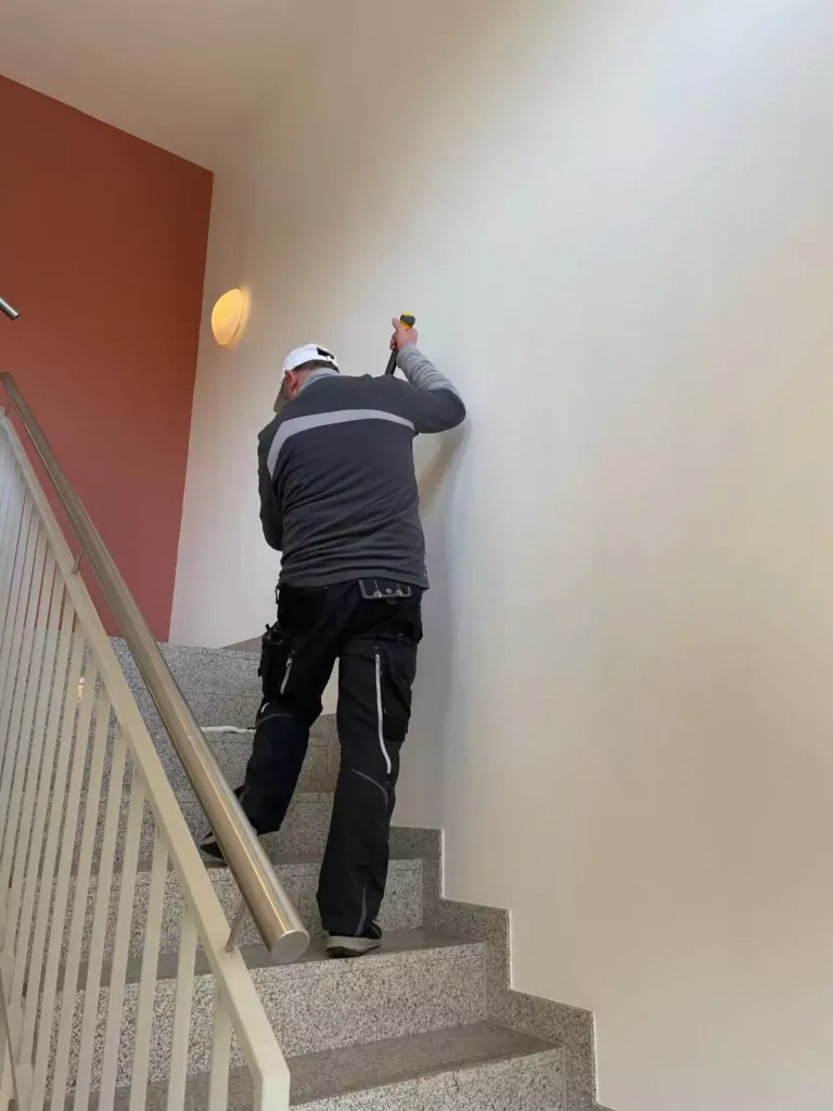 Mitarbeiter reinigt die Wand über einer Treppe im Treppenhaus