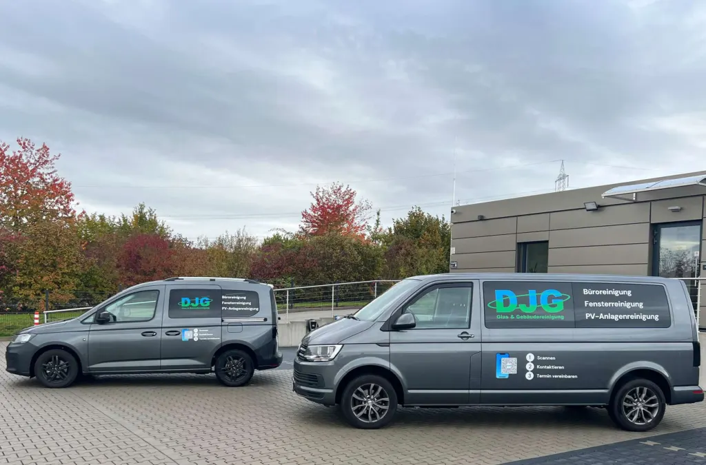 Zwei graue Firmentransporter nebeneinander auf einem gepflasterten Hof