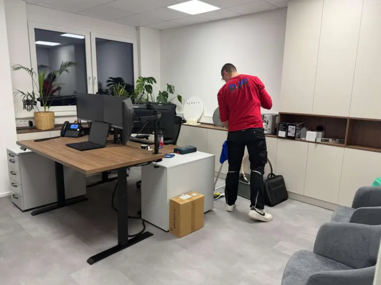 Reinigungskraft säubert ein modernes Büro mit Schreibtisch und Monitoren