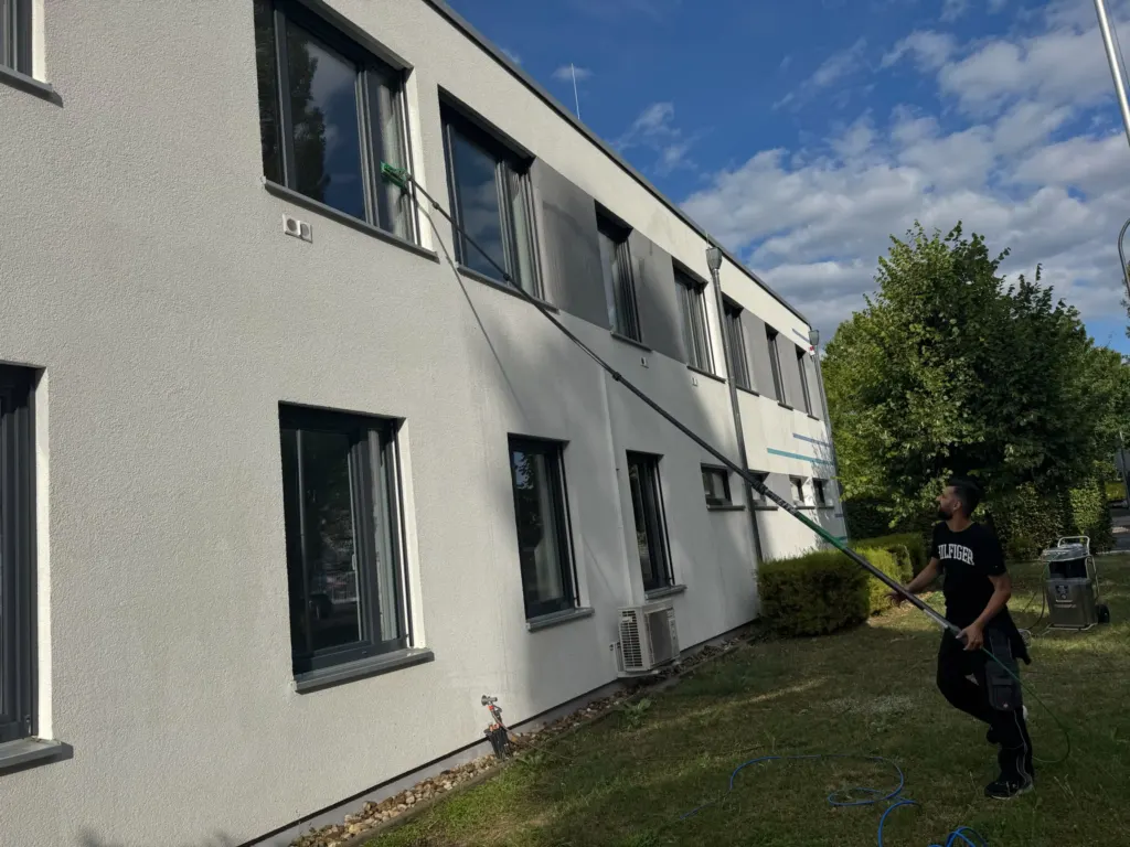 Mitarbeiter reinigt Bürofenster mit wassergeführter Teleskopstange