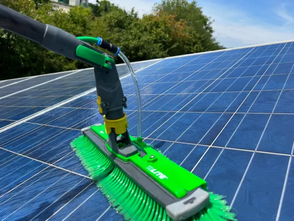 Grüner Waschkopf mit Wasserstrahl auf blauen Photovoltaikmodulen