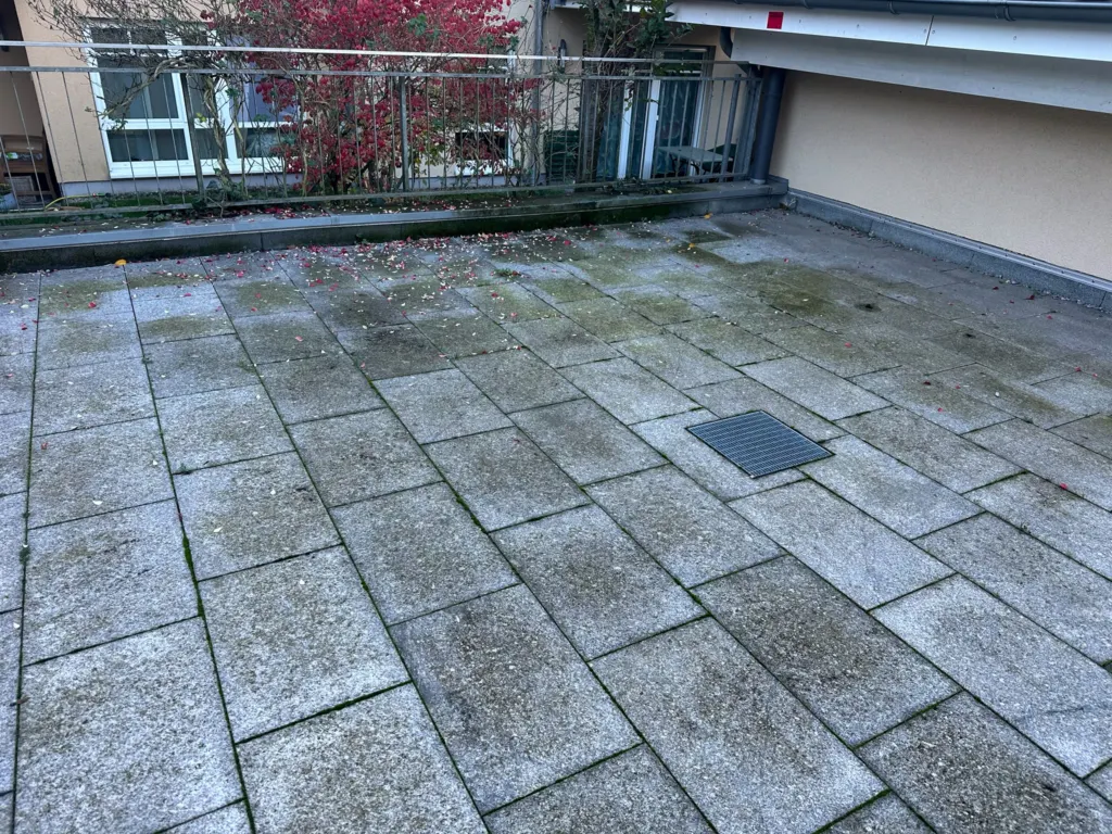 Dachterrasse mit Grünbelag und Laub auf grauen Steinplatten