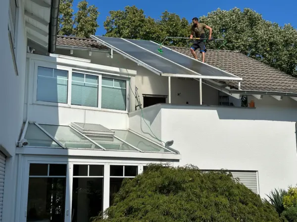 Mitarbeiter reinigt mit Teleskopstange die Glasflächen über einem Wintergarten